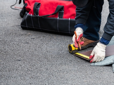 Closeup of construction man measuring roof shingles with tape on