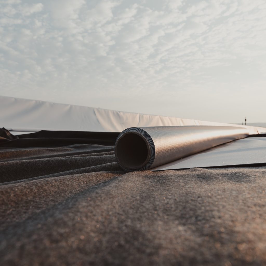 A roll of single ply roofing being unrolled and installed on a rooftop. 